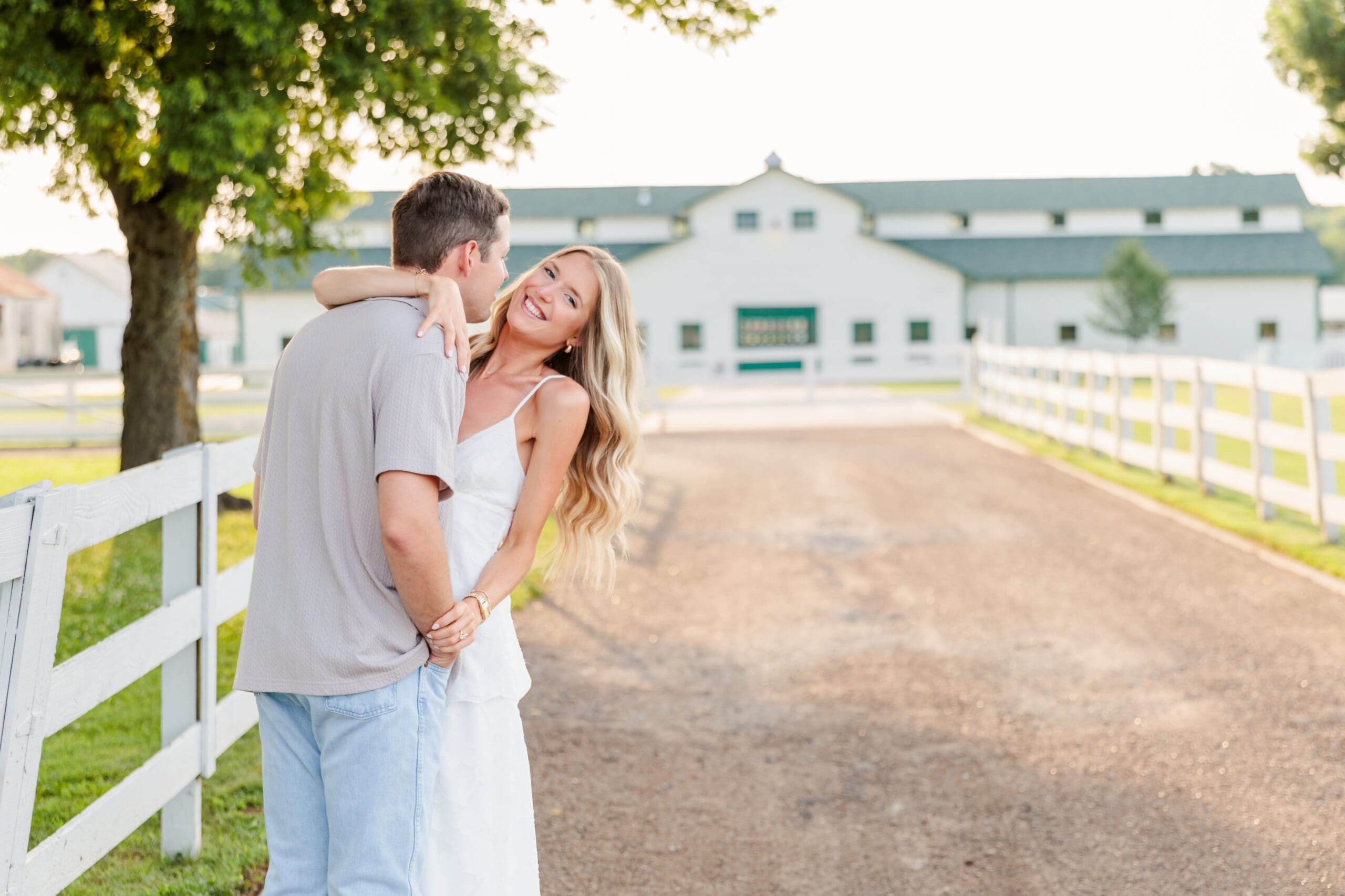 engaged couple embracing on a fence line with barn in the background.
