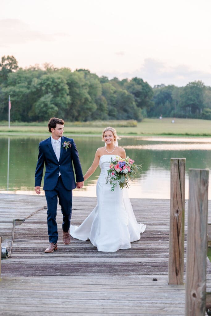 Bride and groom in golden hour light holding hands on a dock on a pond.