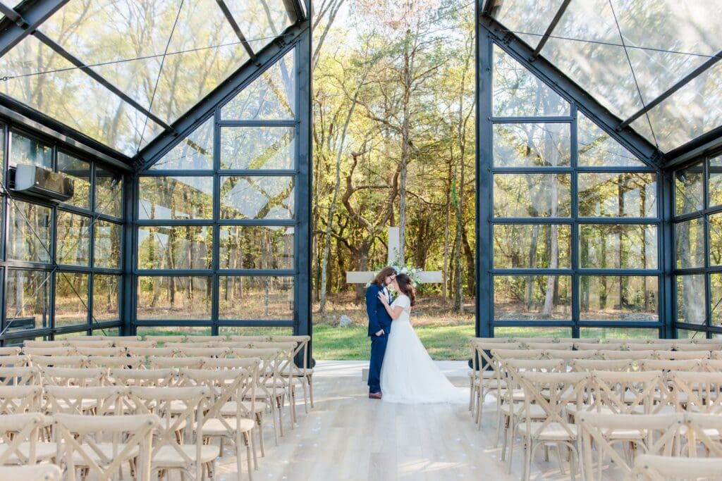 Newlyweds posing together inside the glass chapel at Jubilee Woods