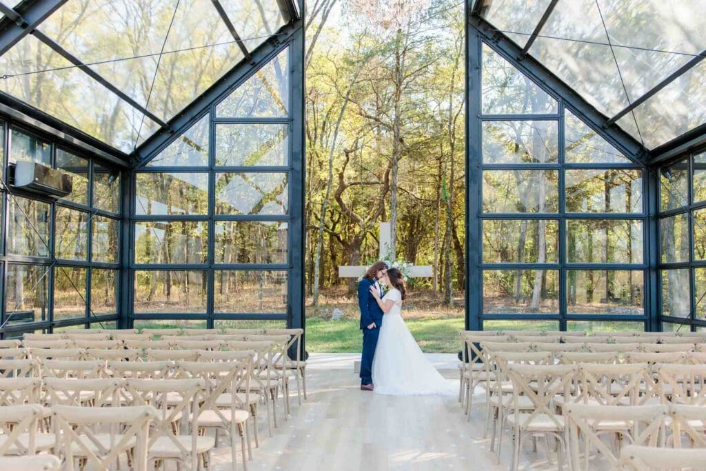 Newlyweds posing together inside the glass chapel at Jubilee Woods